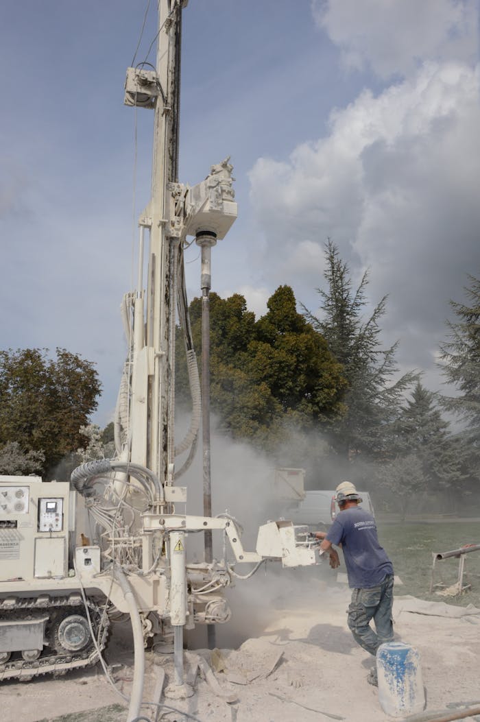 A worker operates a large industrial drilling rig outdoors on a cloudy day.