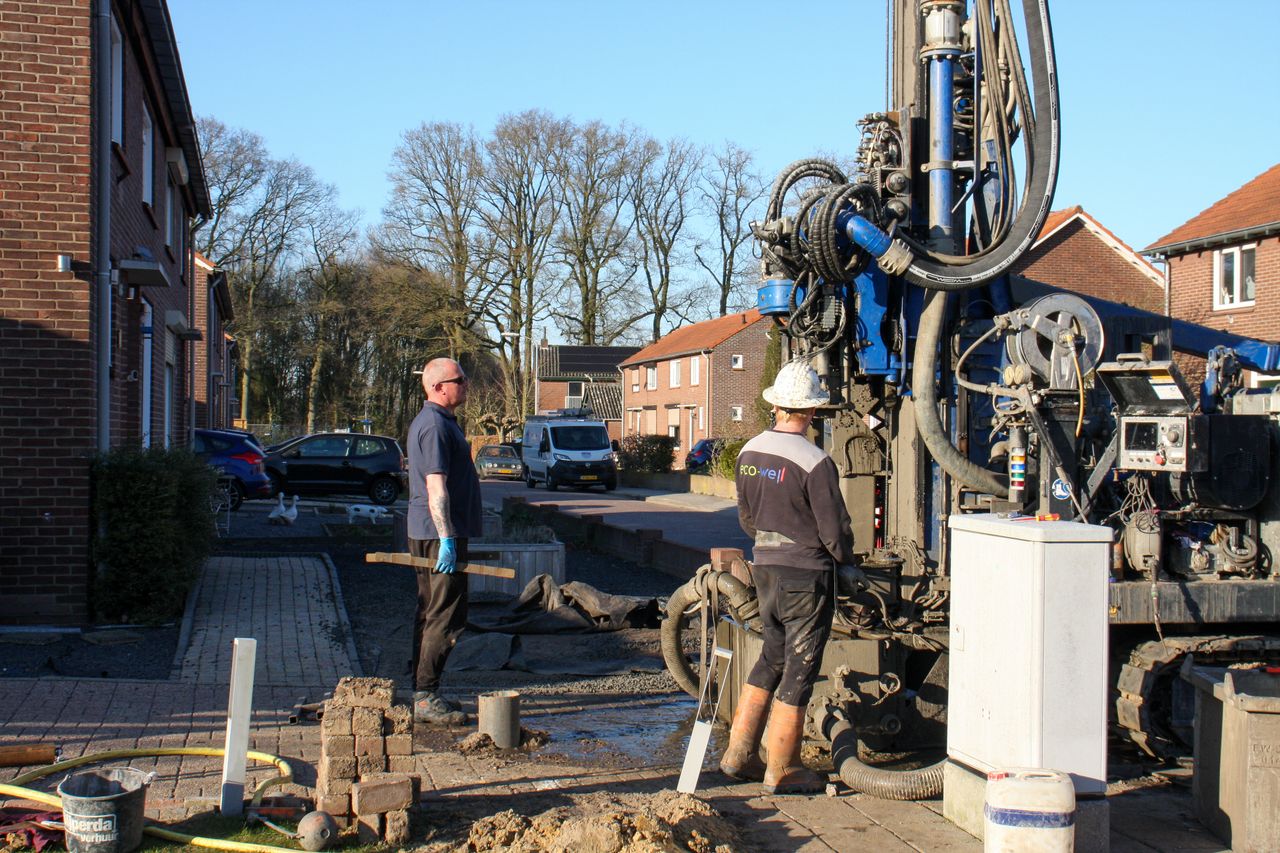 Two construction workers operating drilling equipment on a residential street under clear blue skies.