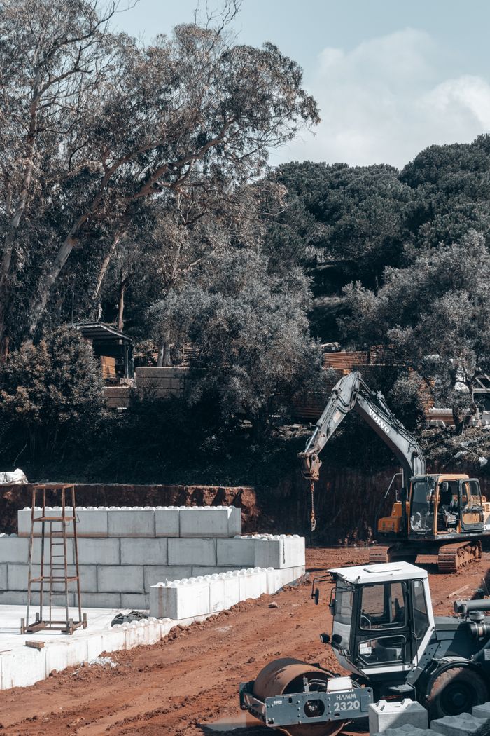 A busy construction site with heavy machinery, soil, and foliage around.